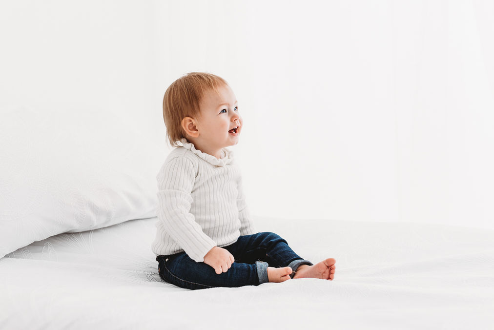 Baby girl sitting on white bed during studio baby photo shoot with Esher photographer Rachel Fairfield Photography