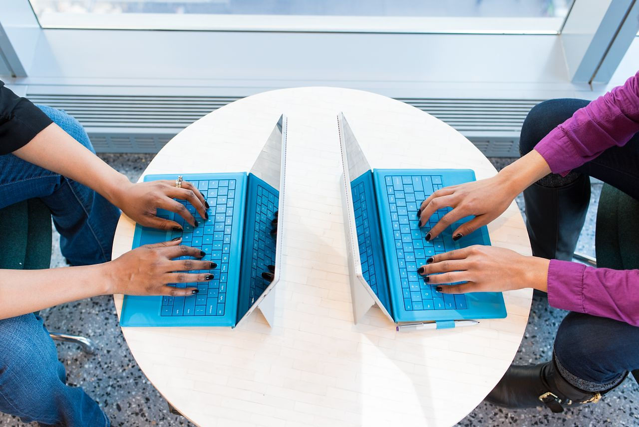 Two small business owners doing their bookkeeping on laptops while AI categorizes transactions