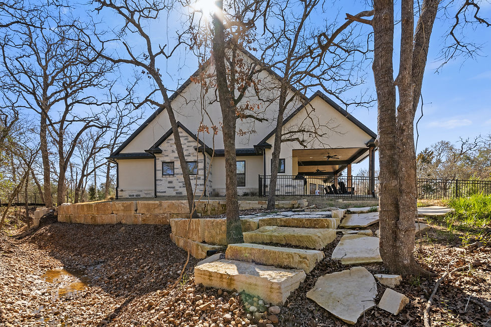 Natural stone retaining wall and steppingstone path leading up to a modern farmhouse-style home surrounded by mature oak trees