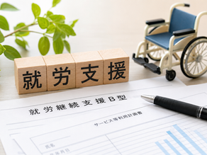 就労継続支援B型事業所の運営と支援体制をイメージした写真。就労支援を示す木製ブロックや書類、車椅子模型が配置され、障害福祉サービスにおける生産活動、工賃向上、運営改善、運営指導対策などを表現している。