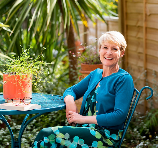 Rebecca Bussy sitting at a table with a book in a sunny garden
