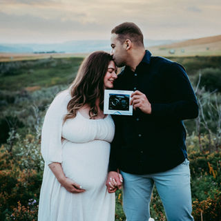 pregnant couple hold up ultrasound while husband kisses' wifes' head in Calgary nw