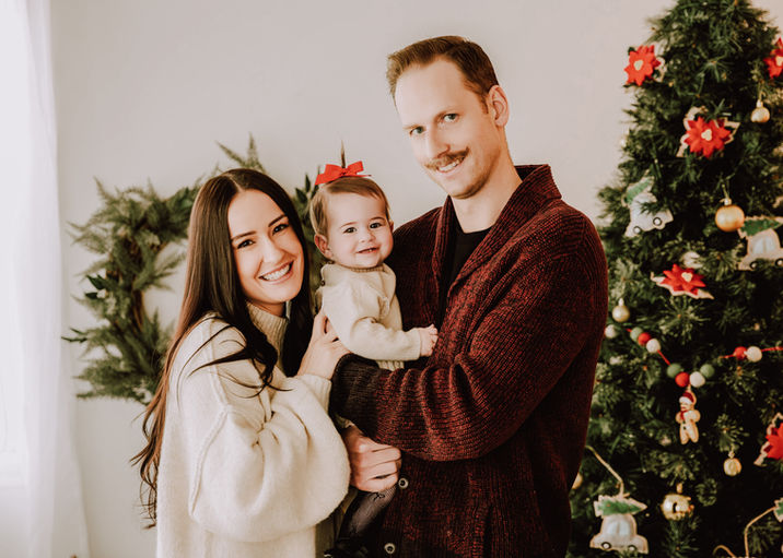 Calgary-couple-hold-their-baby-with-christmas-wreath-behind-them