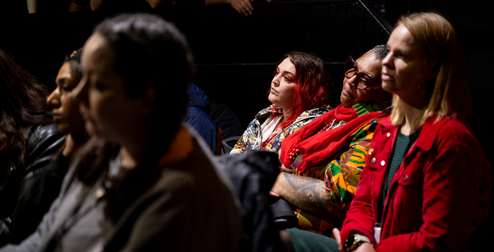 “Participant speaking into a handheld microphone during a panel discussion, seated in front of a green plant wall.”