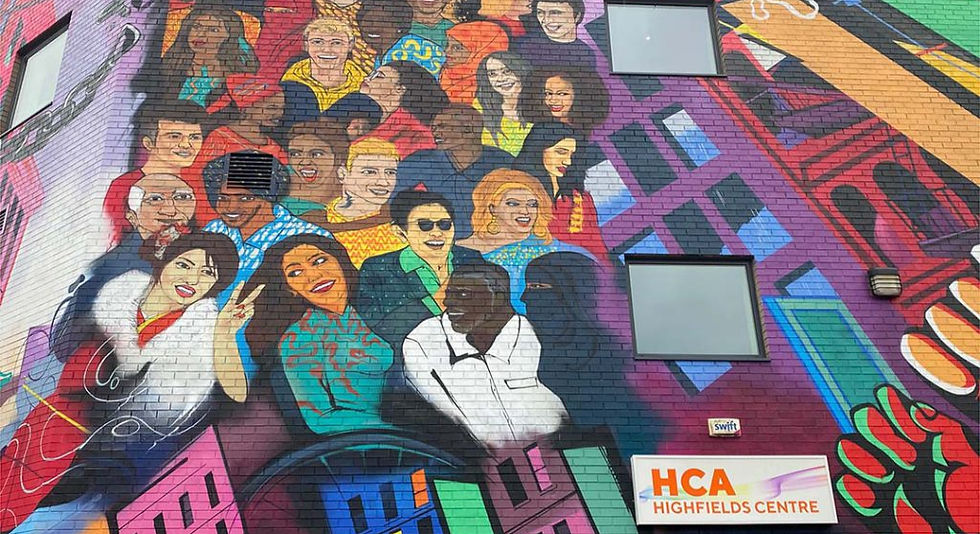 Colorful mural on a building showing diverse people smiling against a vibrant cityscape backdrop. Sign reads "HCA Highfields Centre."
