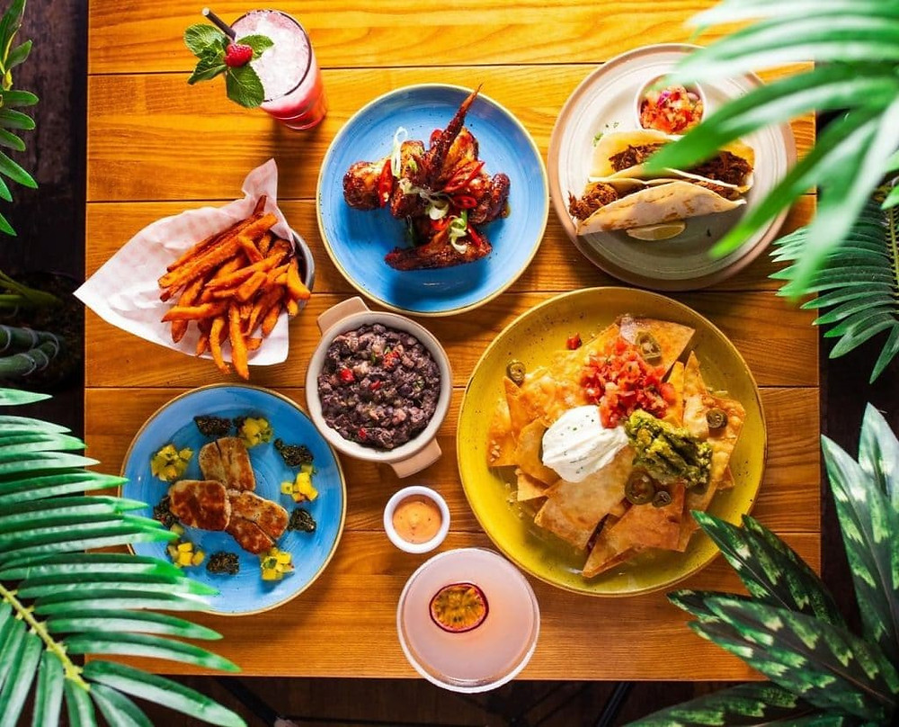 Tapas feast with halloumi, chips, and cocktails on a tropical table at Bodega Cantina restaurant in Leicester
