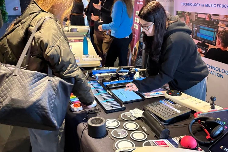 “Hands-on technology demo table with a MIDI keyboard, headphones, and audio gear, with event banners in the background.”