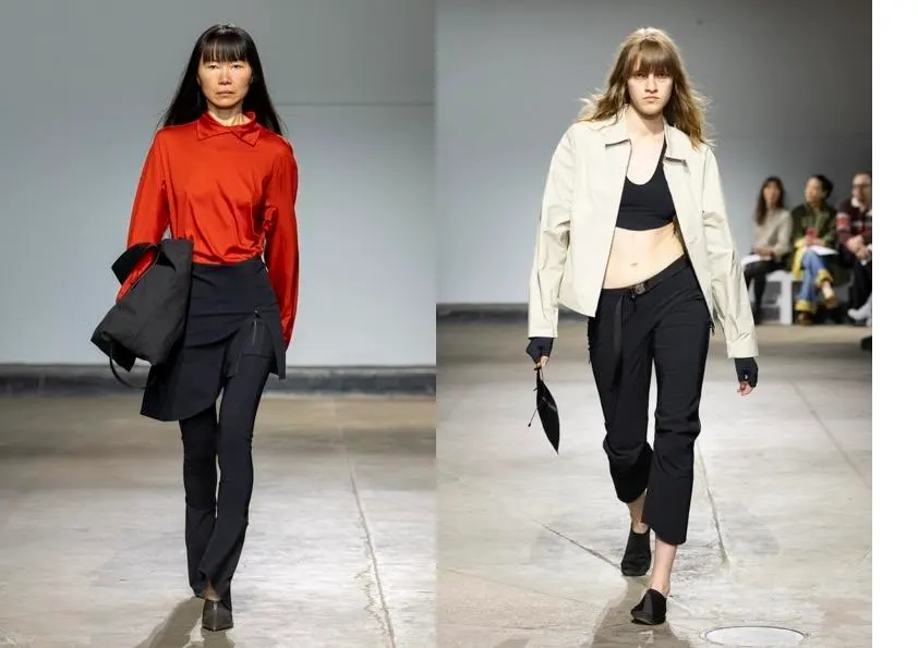 Two models walking the runway at London Fashion Week in tailored minimalist looks – one in a red satin shirt with black trousers, the other in a cropped cream jacket, black bralet and slim black trousers.