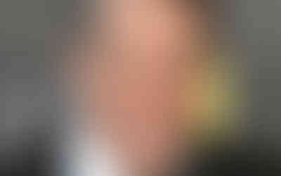 “Close-up of a suited man smiling on a formal red carpet, with a dark backdrop and award logo behind him.”