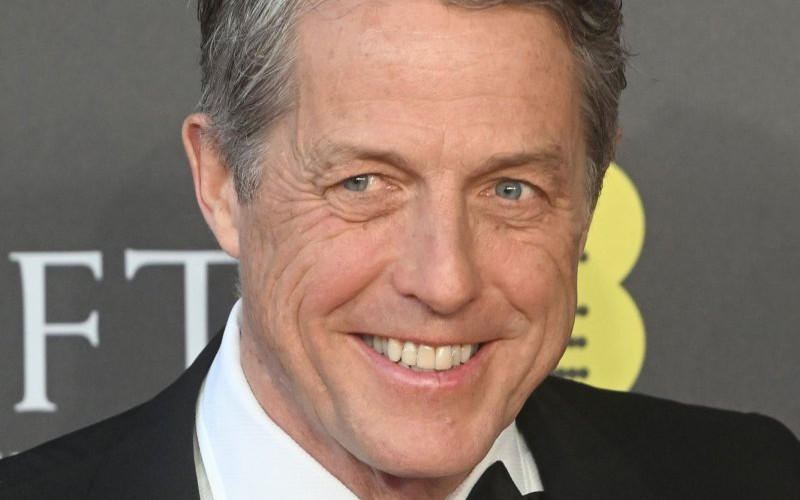 “Close-up of a suited man smiling on a formal red carpet, with a dark backdrop and award logo behind him.”