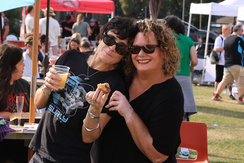 Two people smiling outdoors at Brew Beat Leicester festival. One holds a drink and food. Background tents and crowd. Casual, joyful atmosphere.