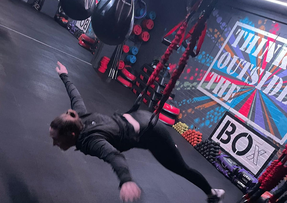 Person suspended in harness, mid-air in gym with colorful "Think Outside the Box" mural, weights, and training gear in background at BOx Fitness Leicester for Bungee Fitness