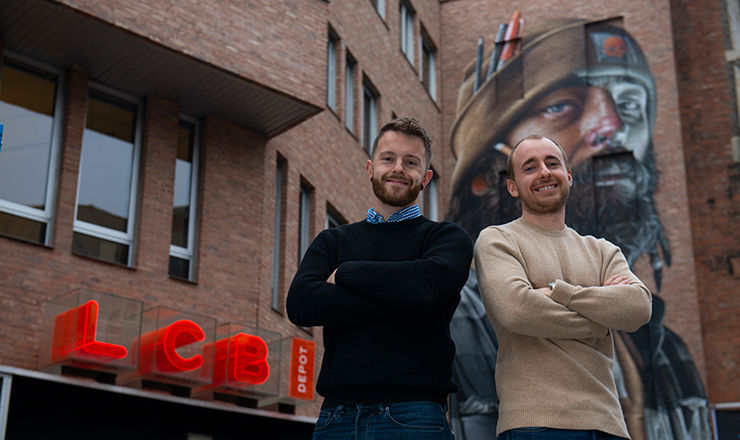 two men smiling stand in front of building with graffiti artwork and red LCB Depot sign