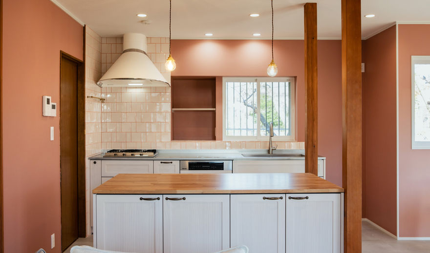 明るいキッチン。白い棚とピンクの壁、木材が特徴的な中古リノベーションの空間。