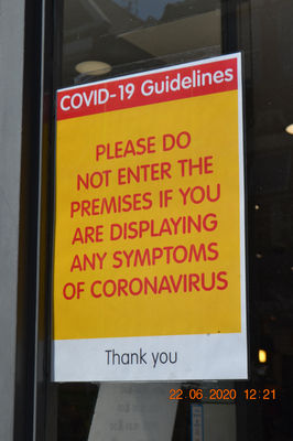 A sign that has a yellow background with red capital text. The text reads "Please do not enter the premises if you are displaying any symptoms of coronavirus" 