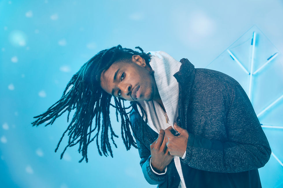 A young man in a hoodie and a jacket on a light blue background. Fake snow floating in the background. A neon snowflake is on the wall.