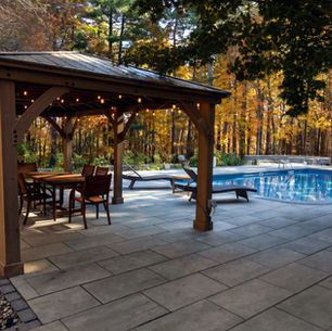 Stone patio and timber pavilion beside a pool with autumn foliage behind