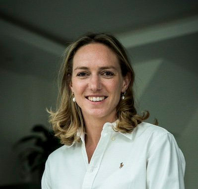 Smiling woman in a white shirt indoors, with a soft gray background and relaxed, friendly expression.