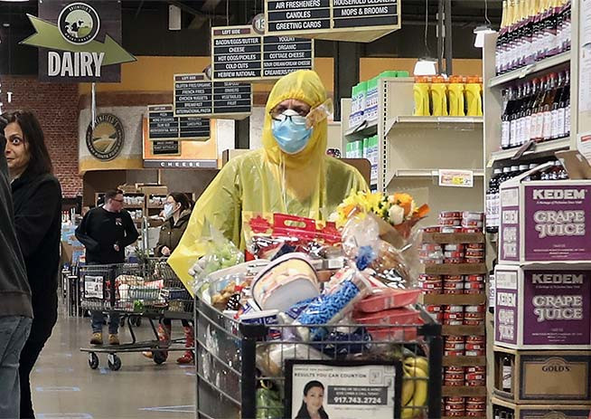 A woman in yellow protective gear pushes a shopping cart in a grocery store.