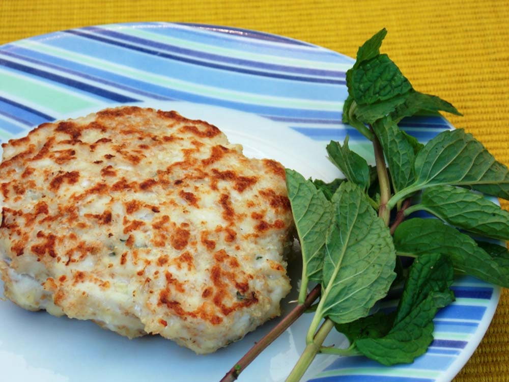 Um prato colorido em tons azuis com um hamburger de frango cozido com folhas de hortelã do seu lado direito enfeitando o prato