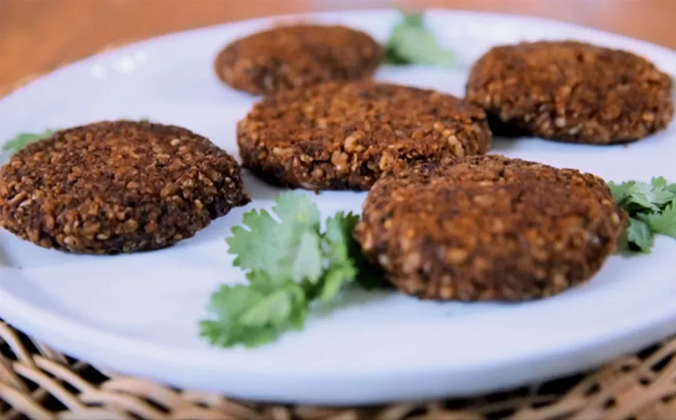 5 hamburgueres de feijão preto em cima de um prato branco com folhas de cebolinha enfeitando em seu entorno.