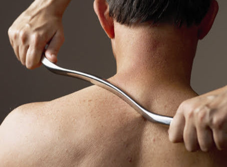 view from back of therapist performing manual therapy on upper shoulder below neck with a graston tool
