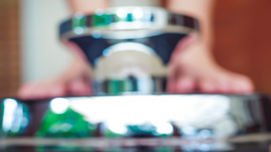 close-up image showing a pink measuring tape lying curled on a wooden floor in sharp focus, with blurred feet standing on a shiny bathroom scale in the background, symbolising weight loss and body measurement.