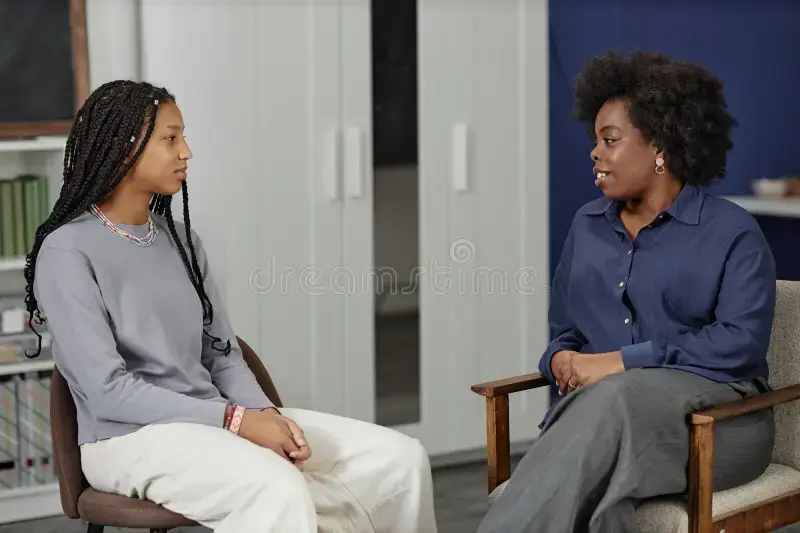 black-woman-talking-to-teen-girl-therapy-session-school-college-side-view-portrait-african