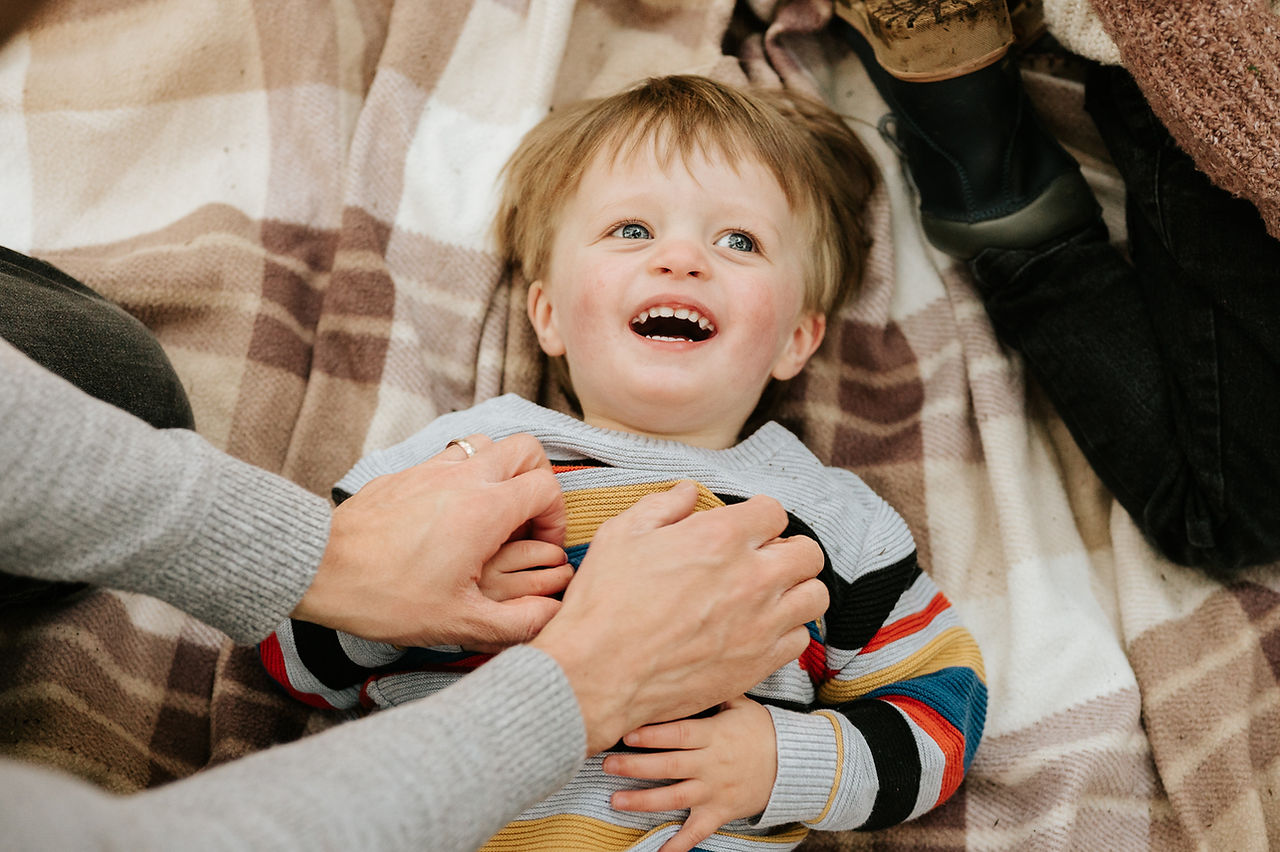 children lay on blanket as parents tickle