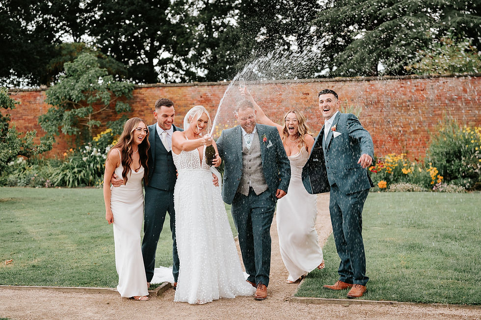 Wedding party spraying champagne in walled garden