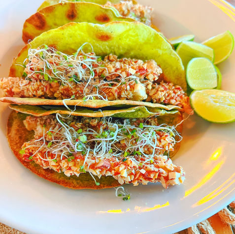 Tacos topped with cheese, avocado, and lime on a round wooden plate.