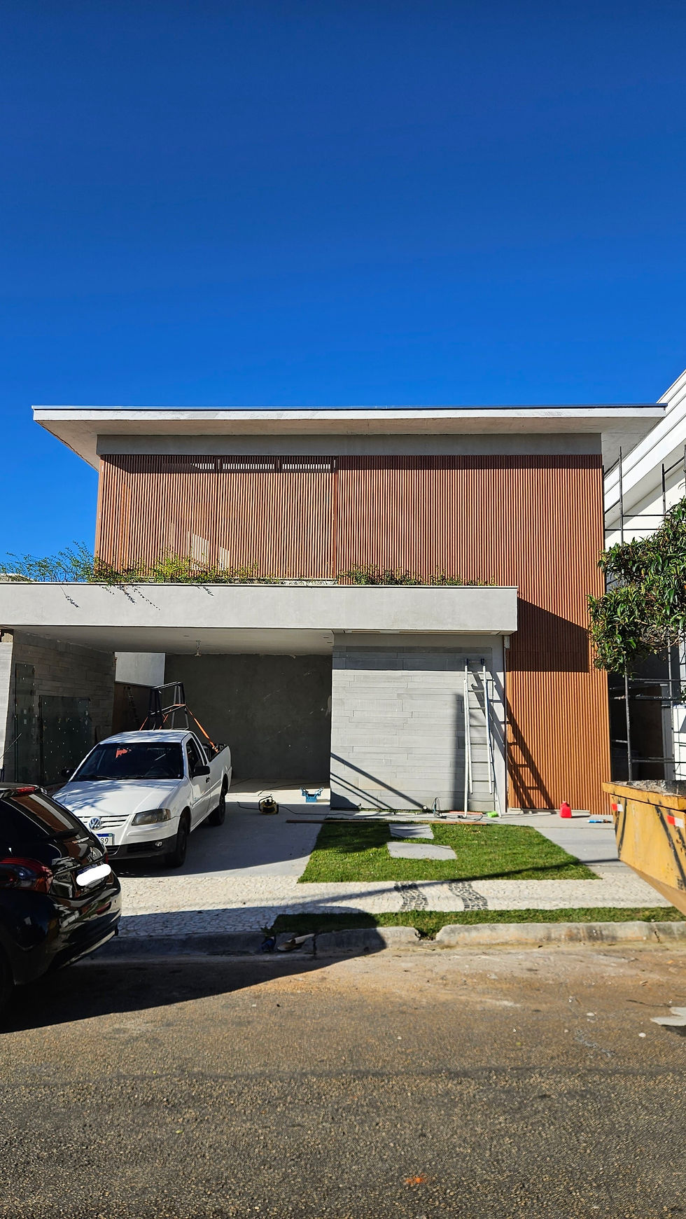 Fachada quase pronta do projeto residencial J | M, desenvolvido pela Duarte Freitas Arquitetura no Granja Anita, em Mogi das Cruzes, mostrando a evolução da obra com volumetria contemporânea, brises verticais e garagem coberta.