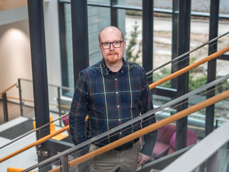 Kuvassa Jarno Karjalainen. Hän on keski-ikäinen mies, jolla on silmälasit, ruudullinen paita ja hän seisoo portaikossa katsoen katsojaa.