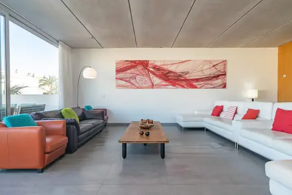 Stilvolles Wohnzimmer im Yoga Retreat Mallorca von Asanyoga – modernes Design mit gemütlichen Sofas, Naturholztisch und kunstvollem Wandbild für entspannte Aufenthalte."