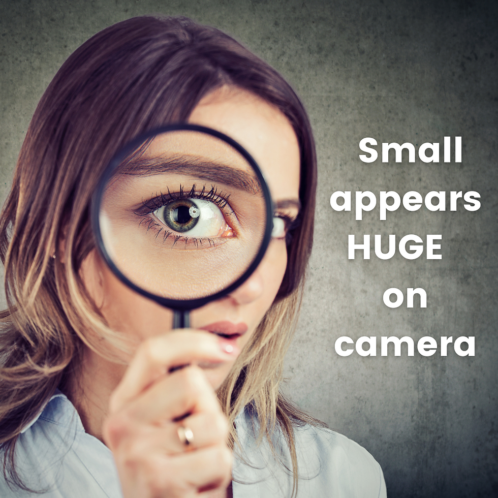 Woman holding magnifying glass enlarging her eye. Text: "Small appears HUGE on camera." Gray background, focus on eye detail.