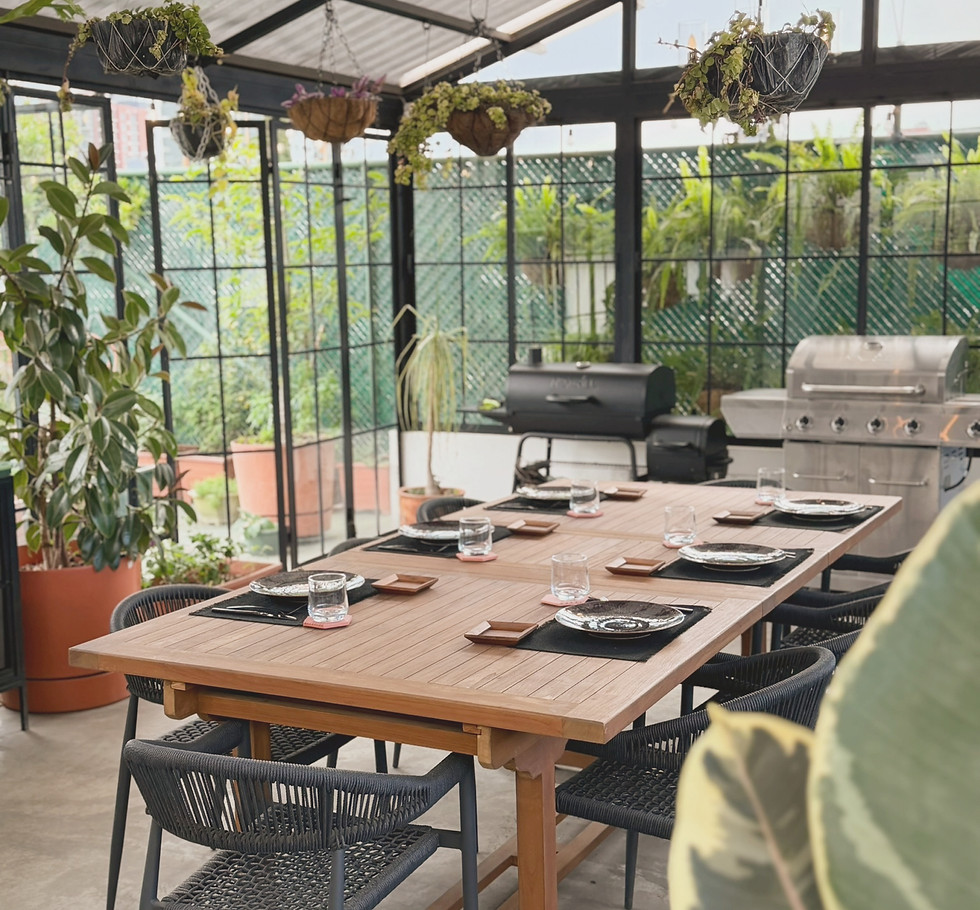 Bright greenhouse-style rooftop with a large dining table, indoor plants and an inviting setting for intimate gatherings in Guatemala City.