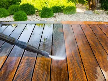 A deck being pressure washed; plants are in the background.