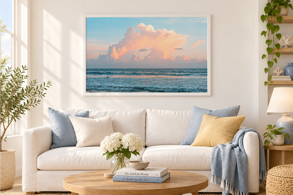 Bright sunlit living room with white sofa, ocean sunset print, and books titled The Kinfolk Home and At Home by the Sea on table.