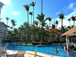 Many tall palm trees at a resort, winding swimming pool and red roof hotel buildings around the pool