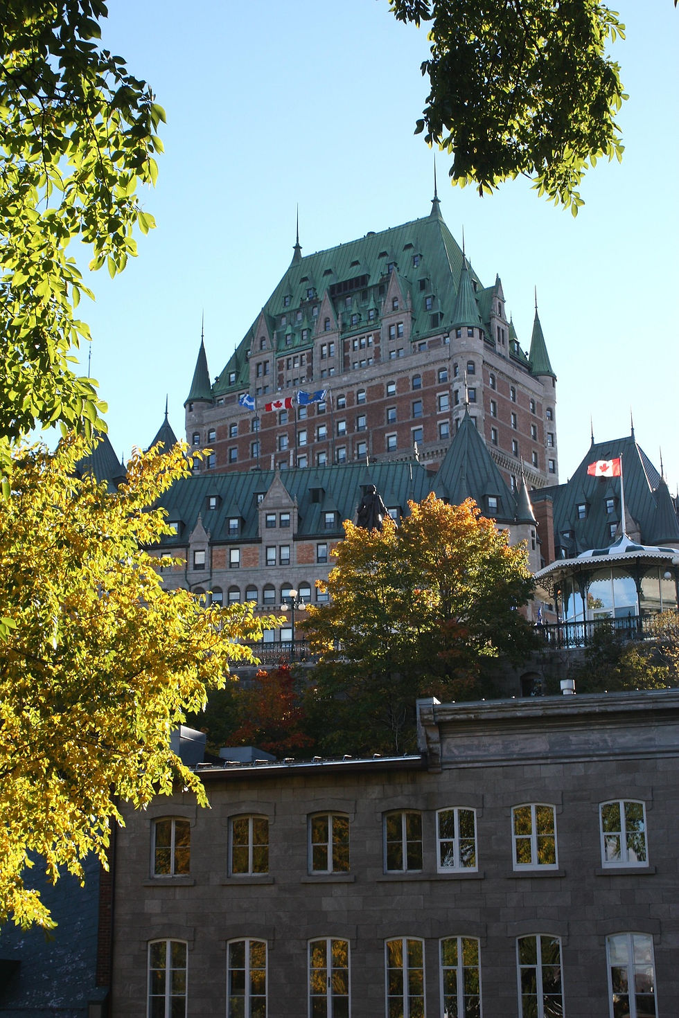 Historic castle-like building with green roofs beneath a clear blue sky, framed by autumn trees, reflecting a peaceful mood.