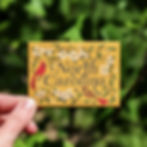 Hand holding a North Carolina souvenir magnet with cardinal and dogwood design outdoors.