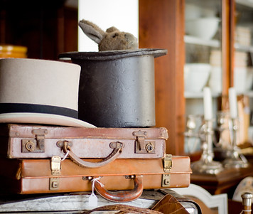 Two antique briefcases and two tophats. A black tophat has a stuffie rabbit peeking out.