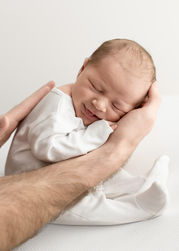 Smiling newborn baby cradled in parent’s hands wearing white babygrow