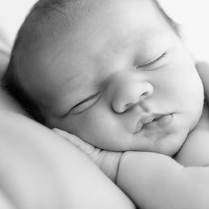 Black and white close-up of newborn baby’s face with eyes closed and hand resting on cheek