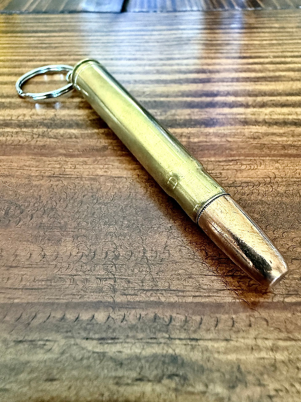.375 H&H MAG brass bullet keychain made from an authentic once-fired cartridge case on a rustic wood background.
