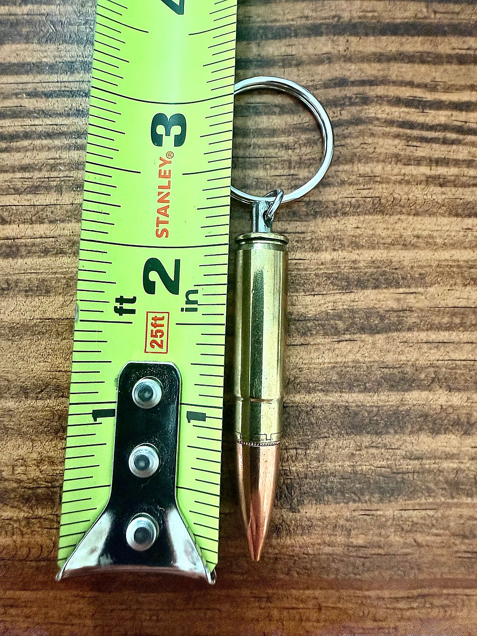 300 Blackout brass bullet keychain shown beside a tape measure for size reference on a rustic wood background.