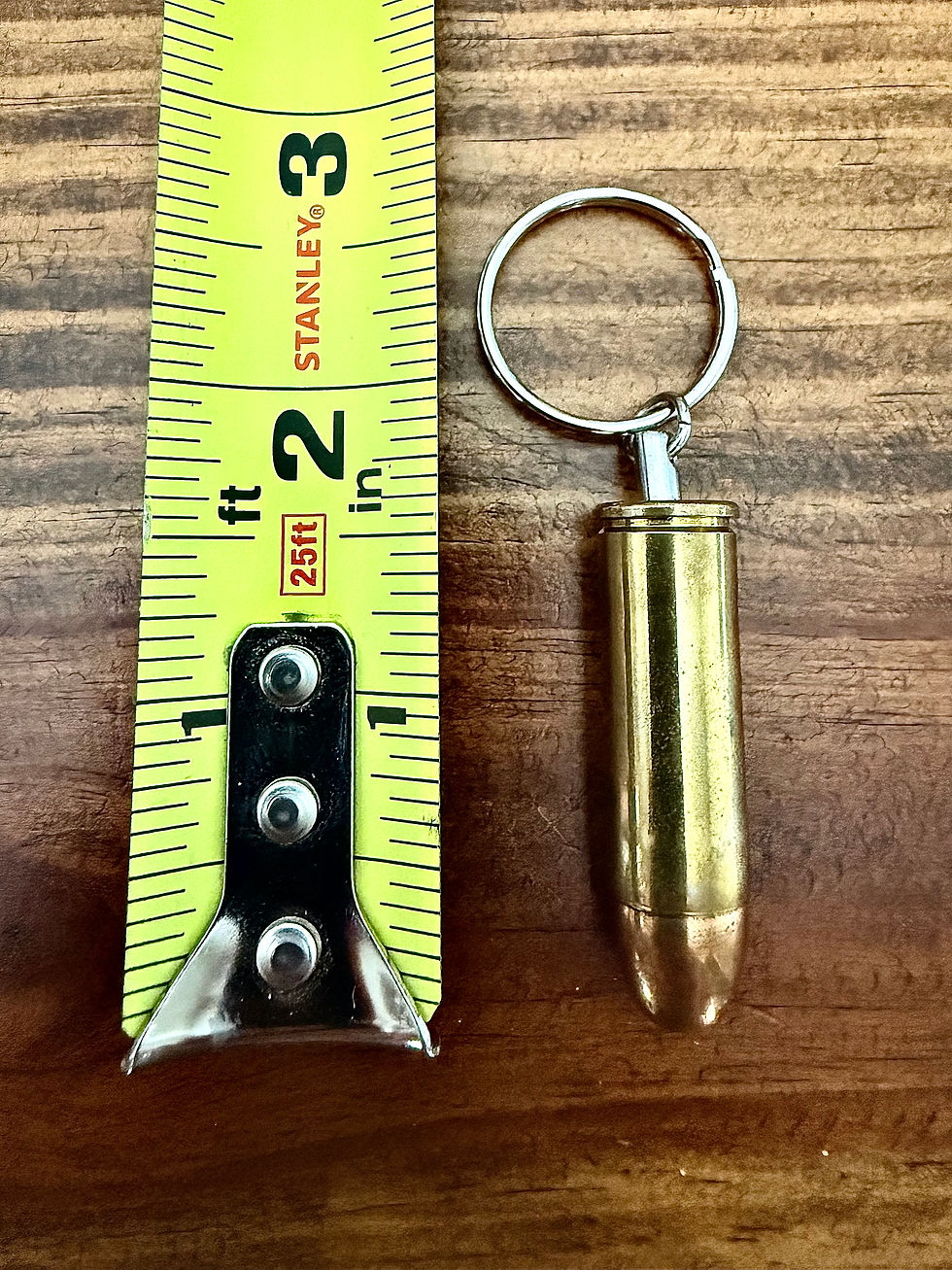 .45 COLT brass bullet keychain shown beside a tape measure for size reference on a rustic wood background.