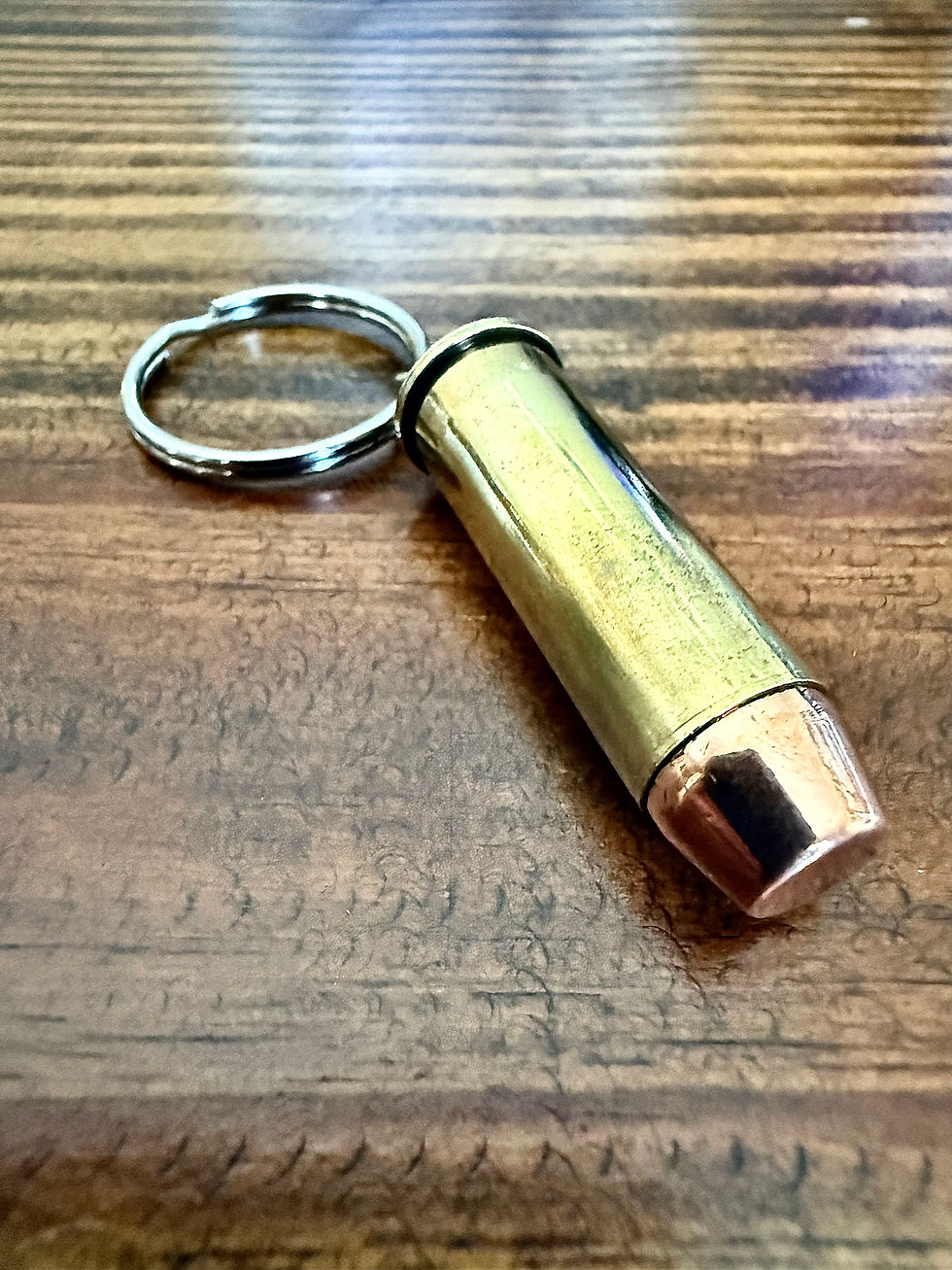 .44 MAG brass bullet keychain made from an authentic once-fired cartridge case on a rustic wood background.
