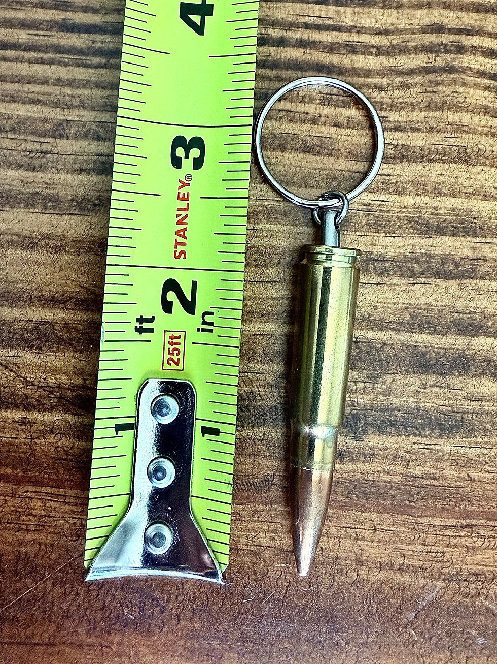 7.62x39mm brass bullet keychain shown beside a tape measure for size reference on a rustic wood background.