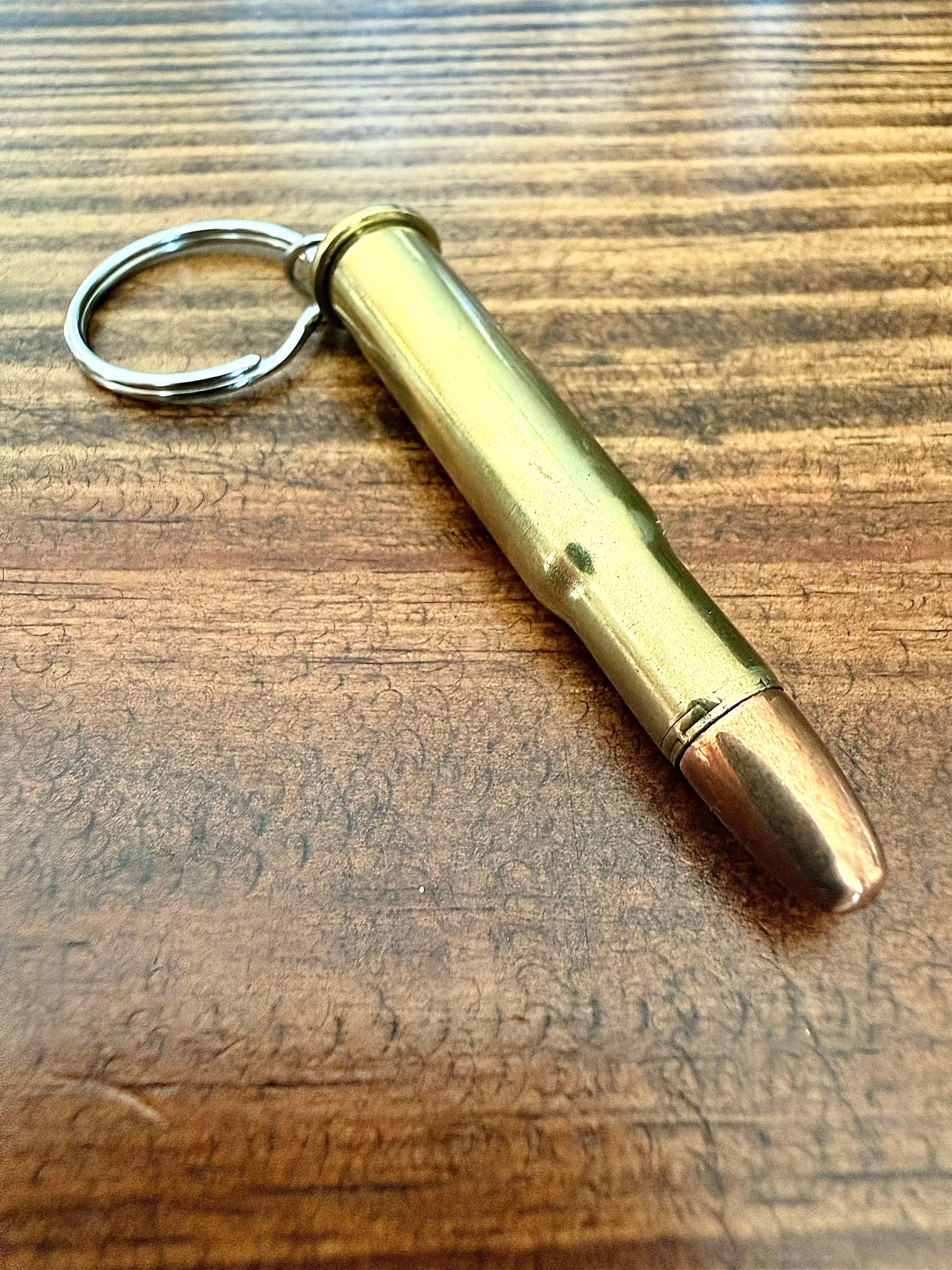 30-30 brass bullet keychain made from an authentic once-fired cartridge case on a rustic wood background.